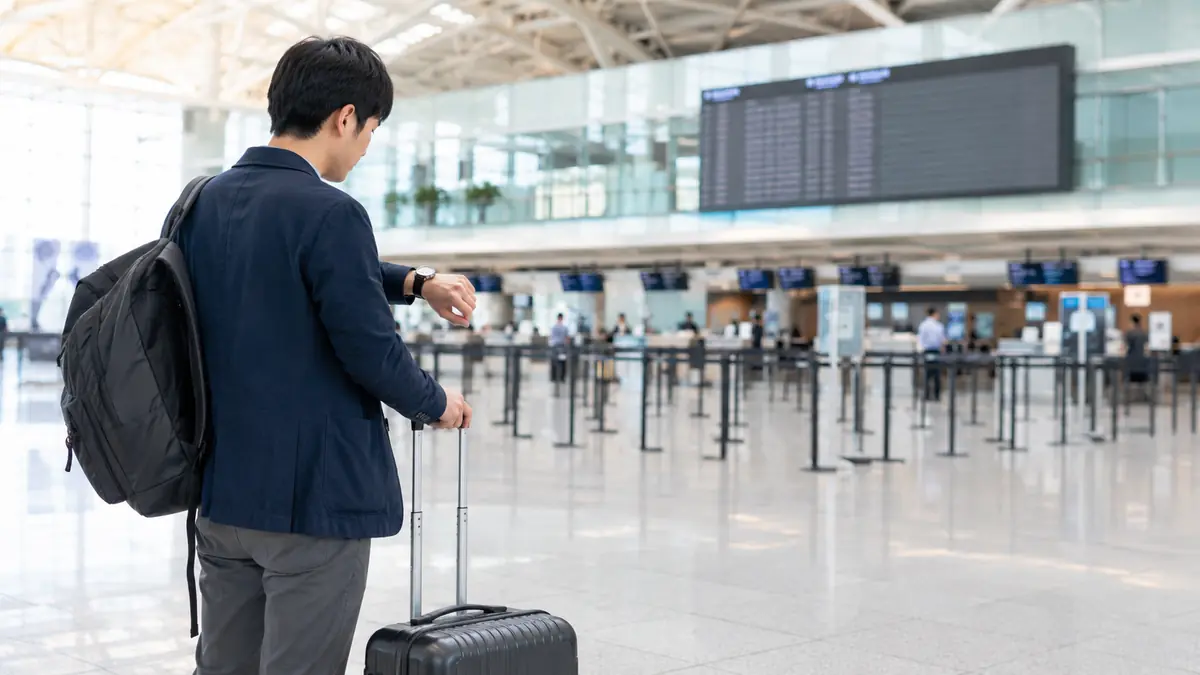 羽田空港の出発ロビーで手荷物締切前に腕時計を確認する日本人旅行者